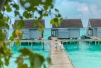 Romantic couple walking hand in hand on a wooden boardwalk with overwater villas in the Maldives.
