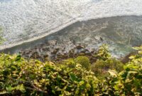 Aerial view of ocean waves crashing on rocks from a cliff in Bali, Indonesia.