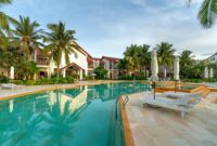A tranquil resort poolside scene with palm trees and white beach chairs for relaxation.