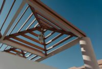 Low-angle view of geometric pergola structure with lanterns against a clear blue sky.