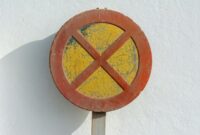 Rusty no parking sign with yellow and red colors mounted on a white wall, showing visible wear and texture.