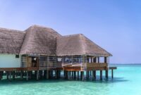 Bubu Villa Tropical Villa Stay Perfect For Island Escapes Stunning overwater bungalow with thatched roof on crystal-clear sea under bright blue sky, perfect for tropical vacations.