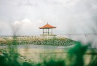 Serene gazebo by the sea on a rocky seashore, under soft daylight sky.