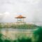 Serene gazebo by the sea on a rocky seashore, under soft daylight sky.